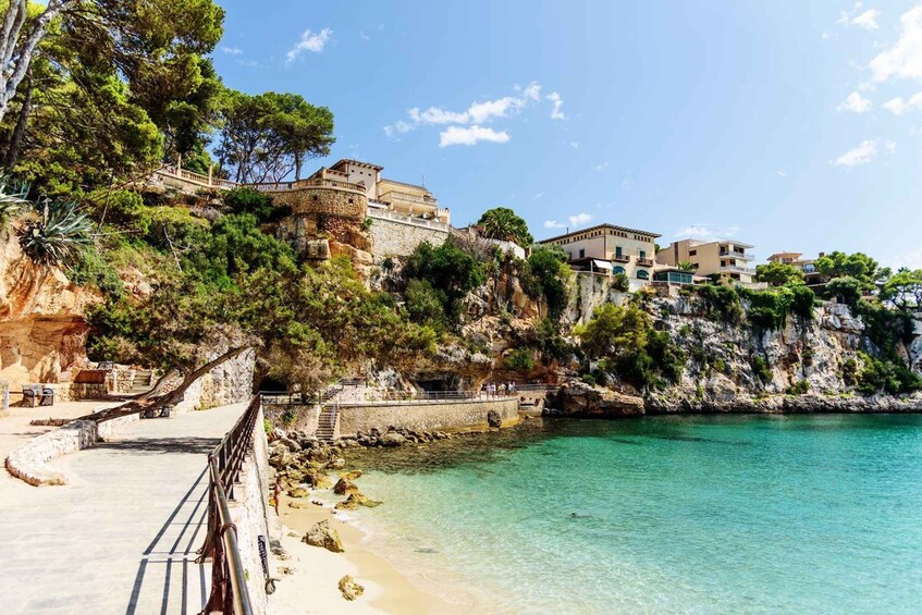 A coastal town with buildings on a cliff, a clear blue sea, and a paved walkway along the shore. 2