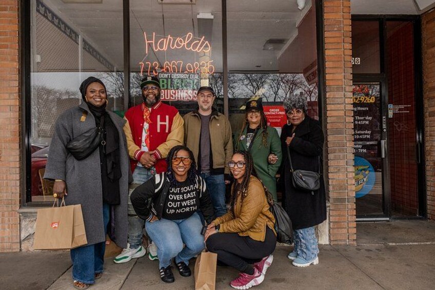 A group of people standing in front of a building with a neon sign that reads 'Harolds 773-467-9935.' 3