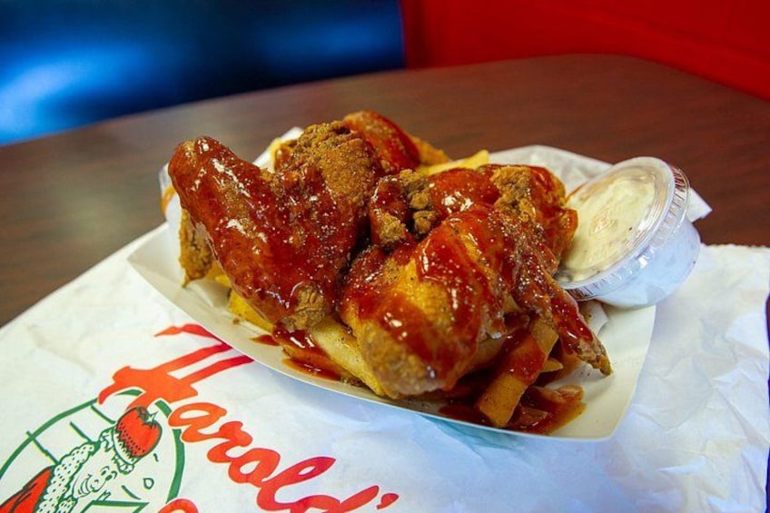 A chicken sandwich with fries and a side of sauce on a paper with a restaurant logo. 5
