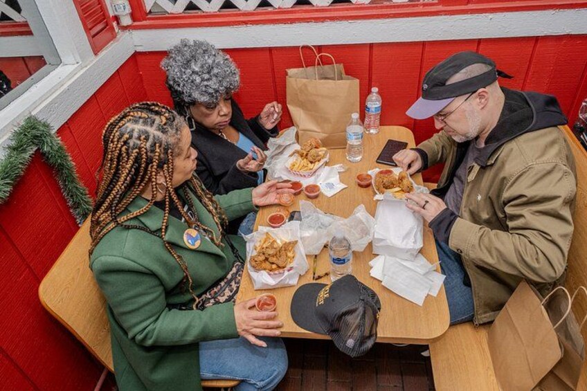 A group of people sitting at a table with food and drinks, in a booth with red and white decor. 5