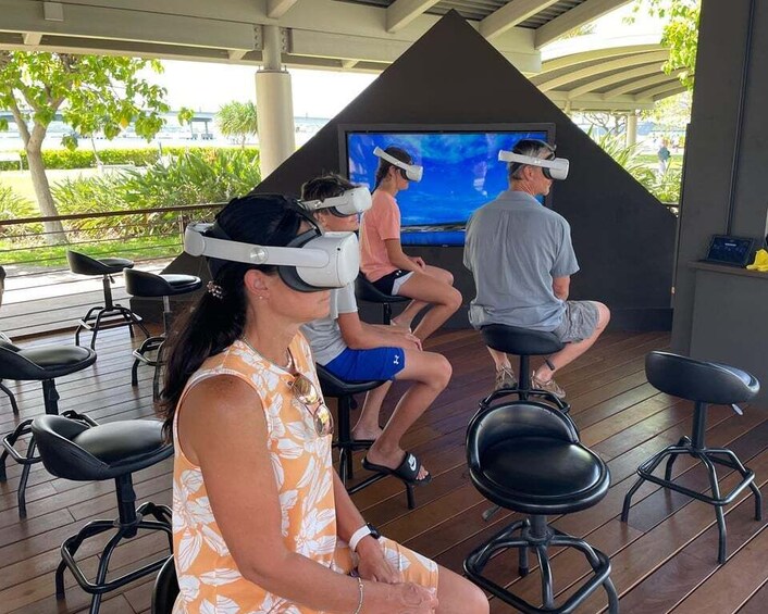 People using virtual reality headsets in an outdoor setting with a large screen and wooden flooring. 2