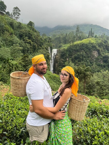 A couple standing in a lush green landscape with a waterfall in the background. 1
