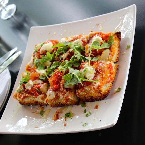 A square plate with a slice of pizza topped with cheese, tomato, and greens. 2