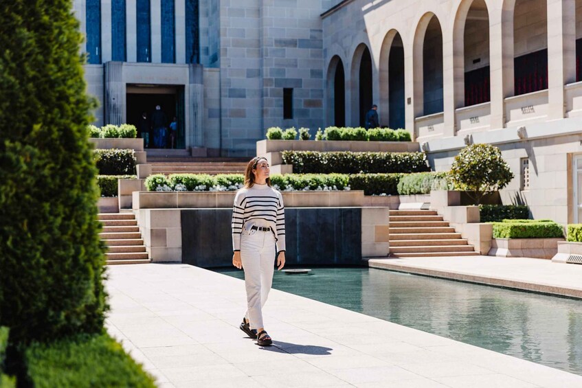 A person walking on a paved path in a courtyard with a pool, surrounded by greenery and classical architecture. 1