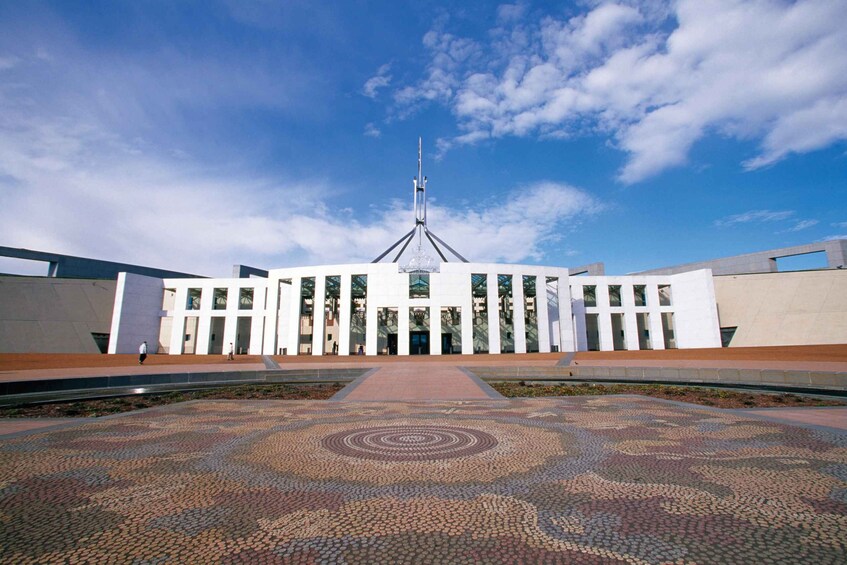 A modern building with a central tower, a patterned pavement, and a clear sky. 2