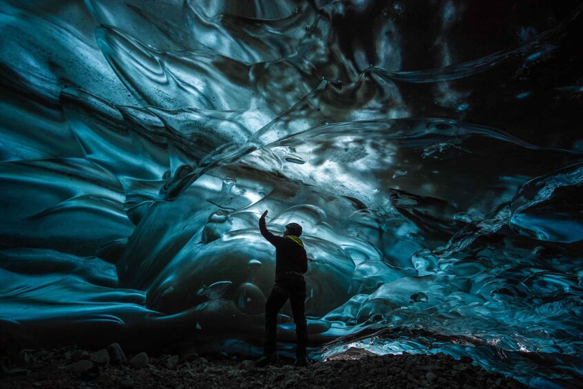 Eine Person steht vor einer großen Eishöhle mit gewundenen Eisformationen. 3