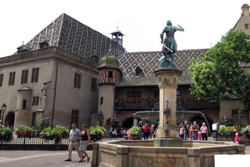A historic building with a tiled roof, a statue on a pedestal, and a fountain in the foreground. 4