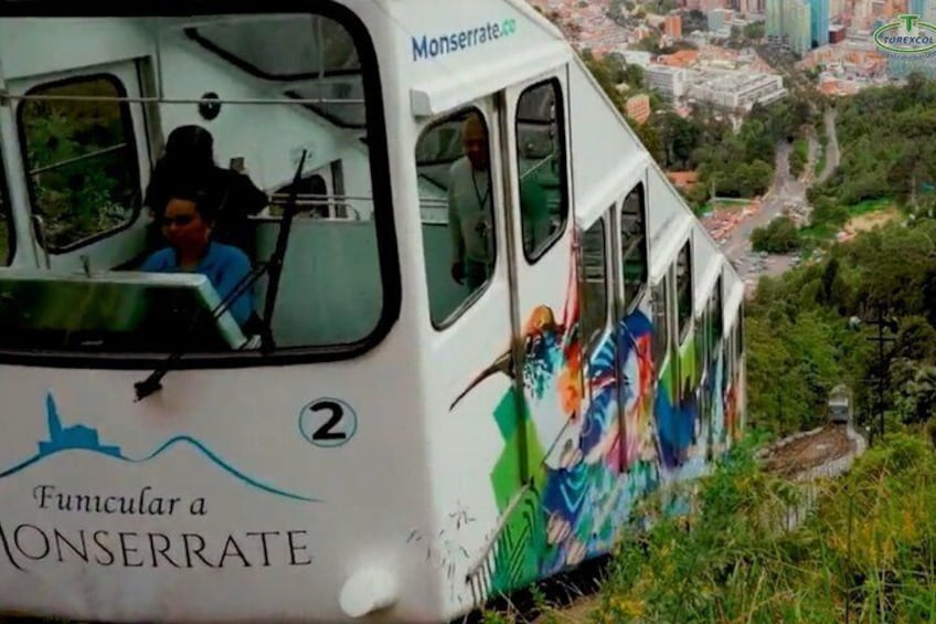 A cable car with 'Fumicular a ONSERRATE' and 'Monserrat.co' on its side, traveling over a lush green landscape with a city in the background. 3