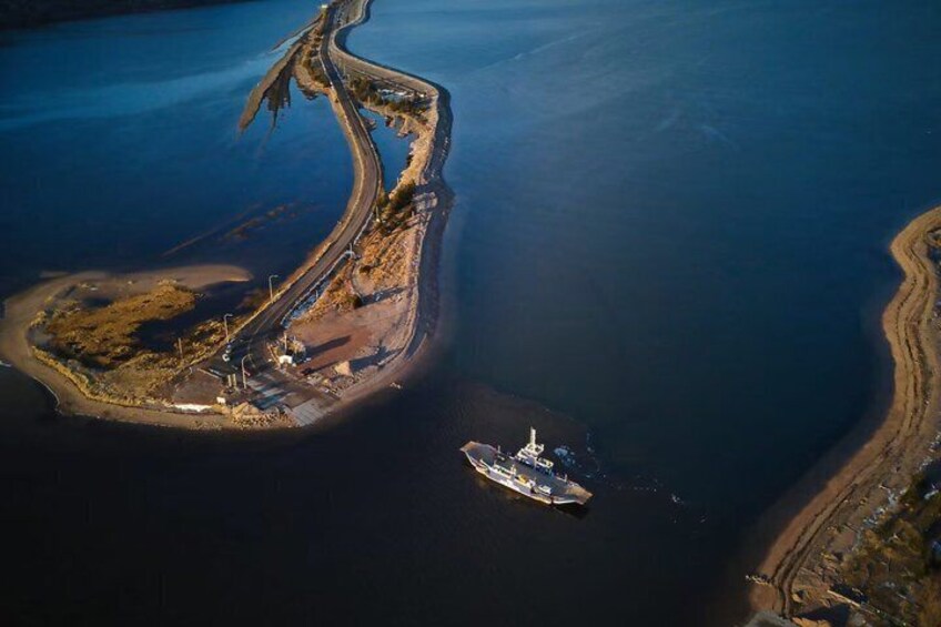 An aerial view of a coastal area with a curved road, a boat, and a small island with buildings. 1