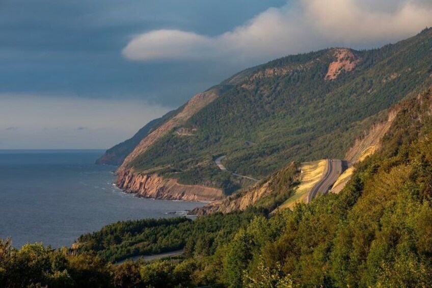 A coastal road winding through a mountainous landscape with dense forests and a view of the ocean. 2