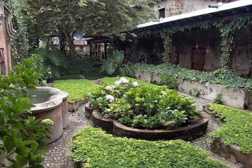 A garden with a circular flower bed, a stone fountain, and a brick wall with climbing plants. 3
