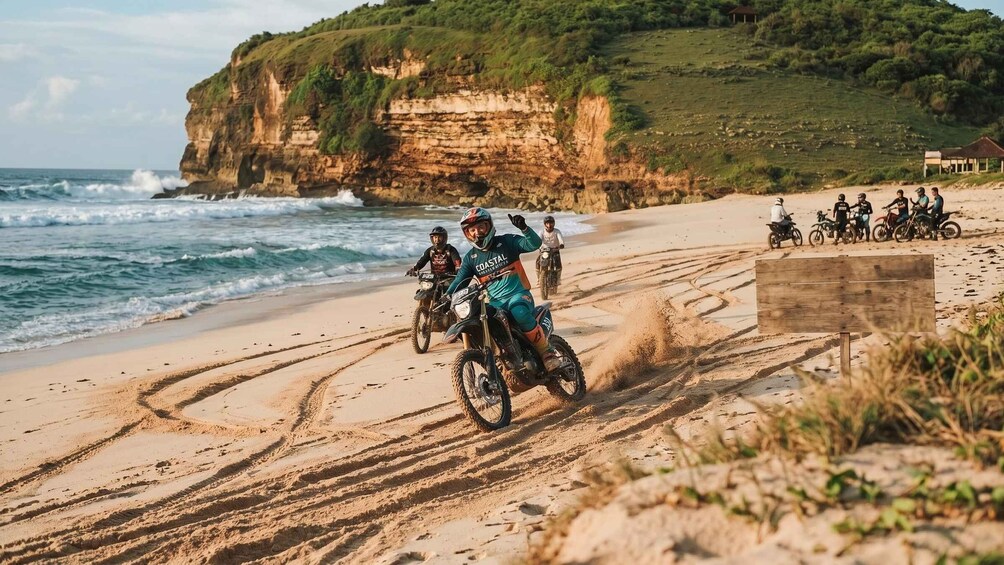 A group of motorcyclists on a sandy beach with ocean waves and cliffs in the background. 4