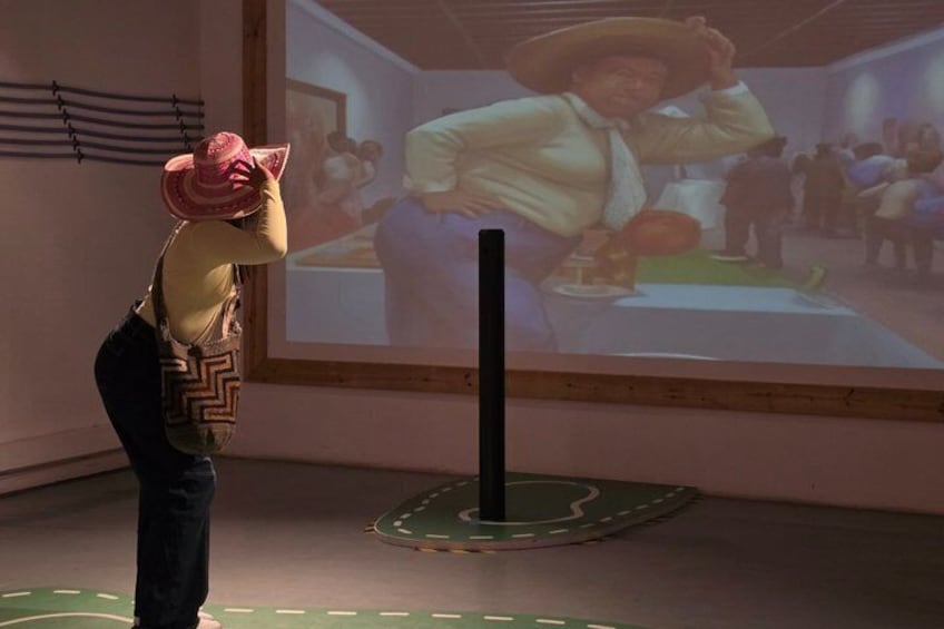A person in a cowboy hat and vest standing in front of a projection screen displaying a scene with a person in a cowboy hat. 5