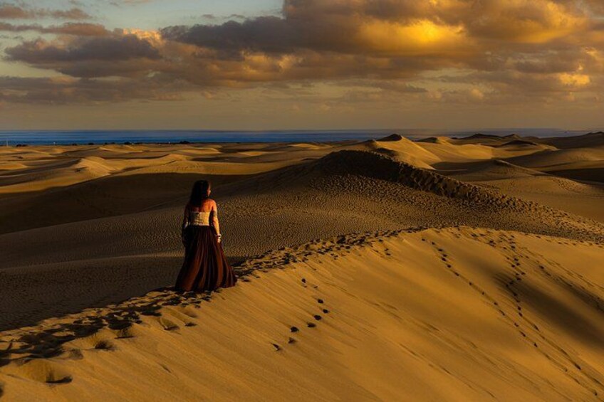 A person standing on a sand dune with footprints leading towards the ocean. 5