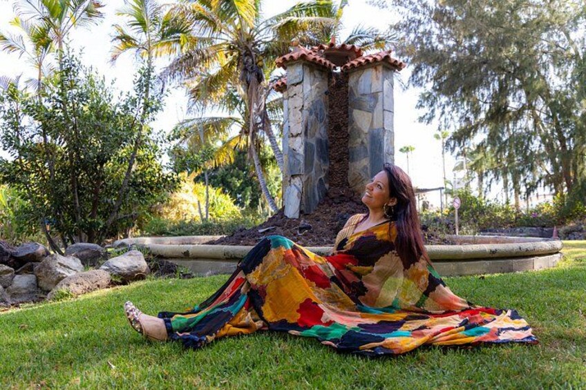 A person sitting on grass with a colorful dress, surrounded by greenery and a stone structure. 2
