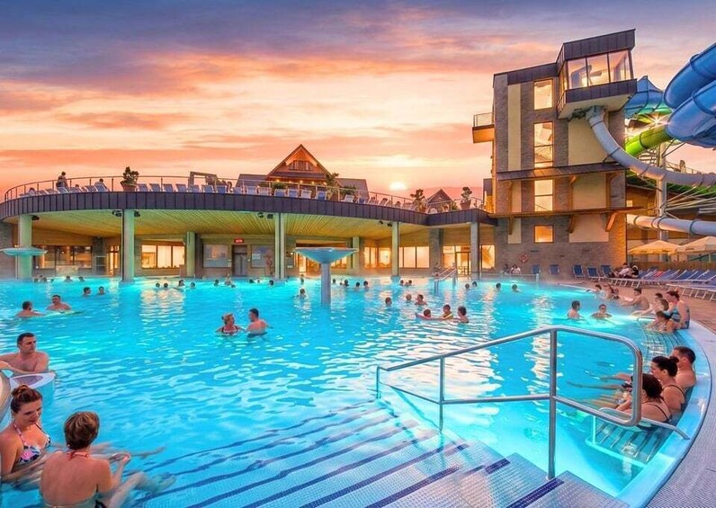 A swimming pool with people, a water slide, and a building with a sloped roof. 1