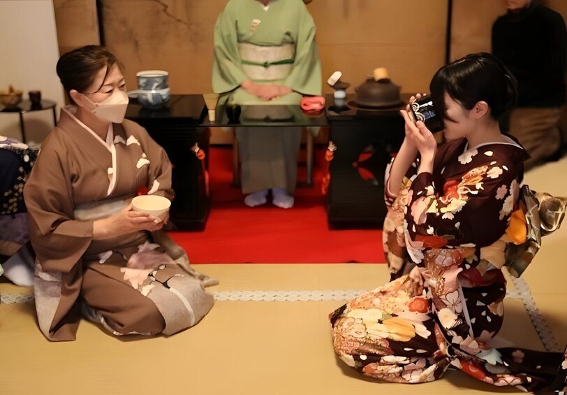 Two people in traditional attire, one holding a bowl, seated on tatami mats. 4