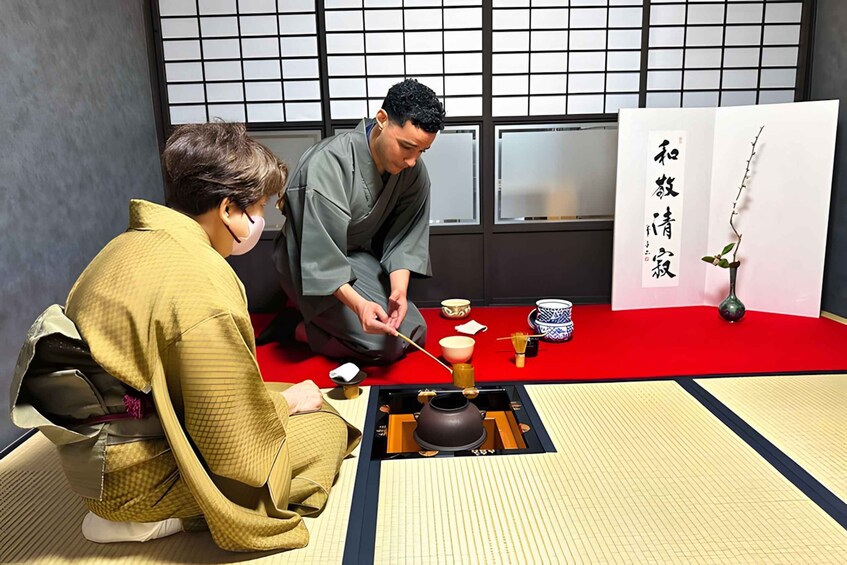 Two individuals performing a tea ceremony with traditional Japanese utensils and a tatami mat floor. 3
