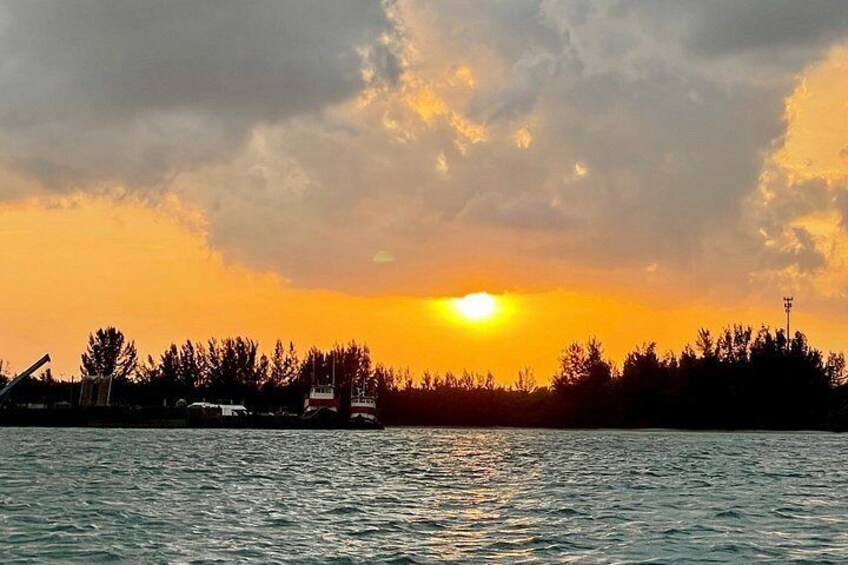A sunset over a body of water with a silhouette of trees and a distant building. 2