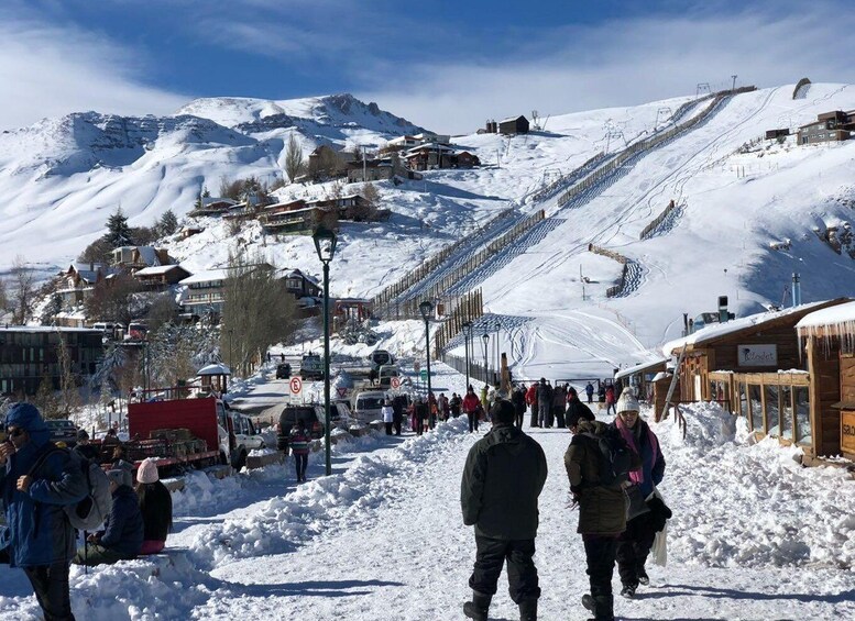 A snowy mountain town with a ski slope, buildings, and people walking. 1