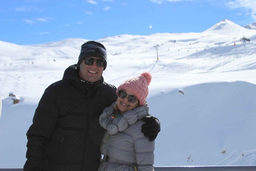 Two people in winter clothing, a snowy mountain landscape, and a ski lift in the background. 2