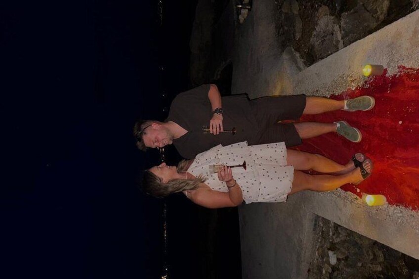 Two people standing on a red carpet with a rocky background. 2