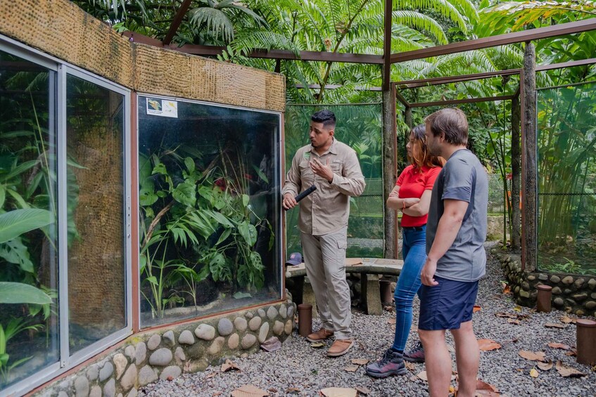 A man in a beige uniform standing next to a large aquarium, with two people conversing nearby. 2