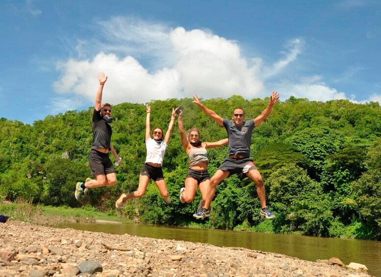 Four people jumping in mid-air with a river and dense greenery in the background. 3