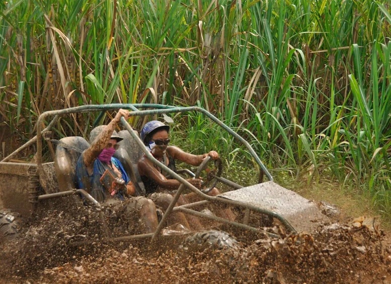 Two people in a makeshift vehicle navigating through a muddy field with tall vegetation. 1