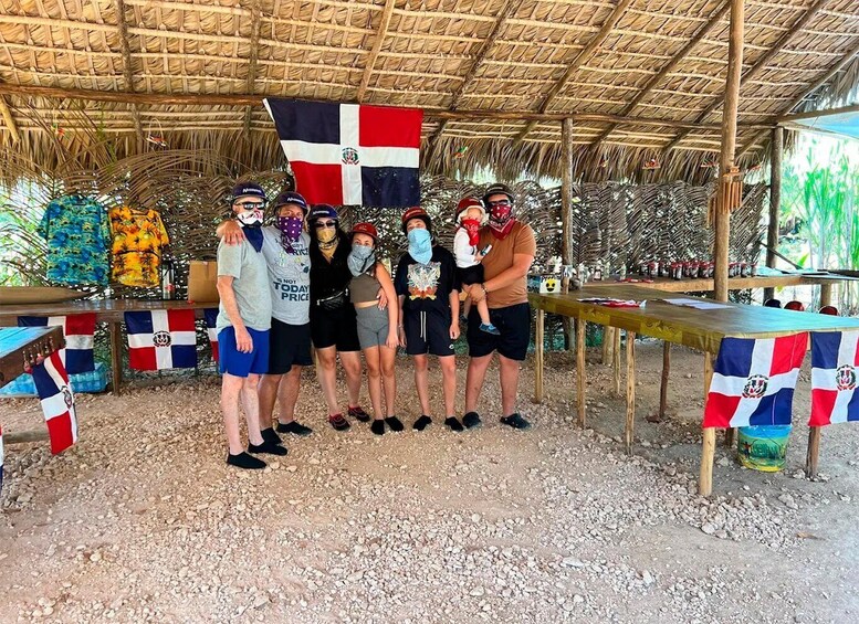 A group of people posing under a thatched roof structure with a flag, surrounded by tables with flags and tropical-themed decorations. 4