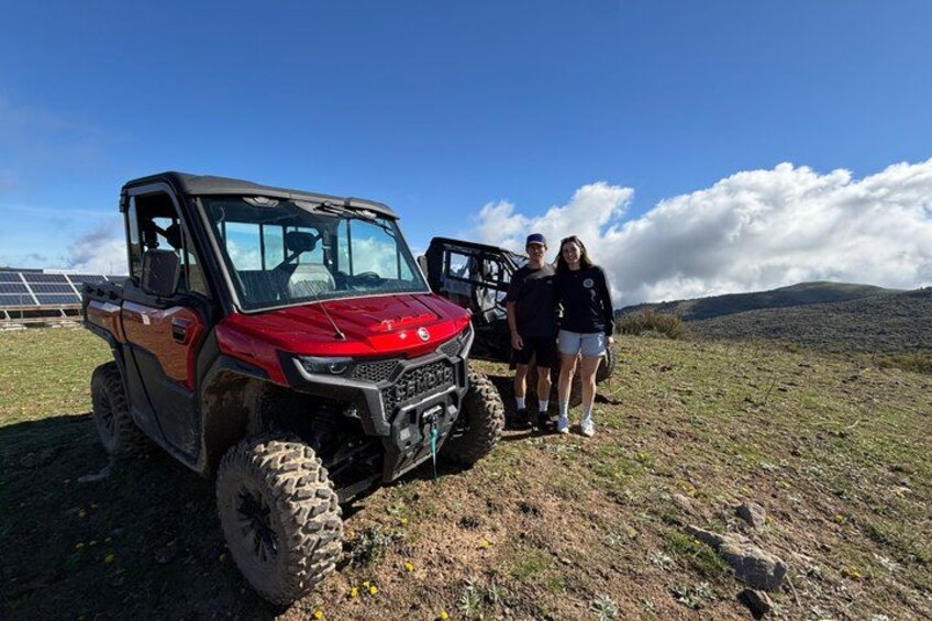 A red off-road vehicle parked on a grassy field with a mountainous background. 4