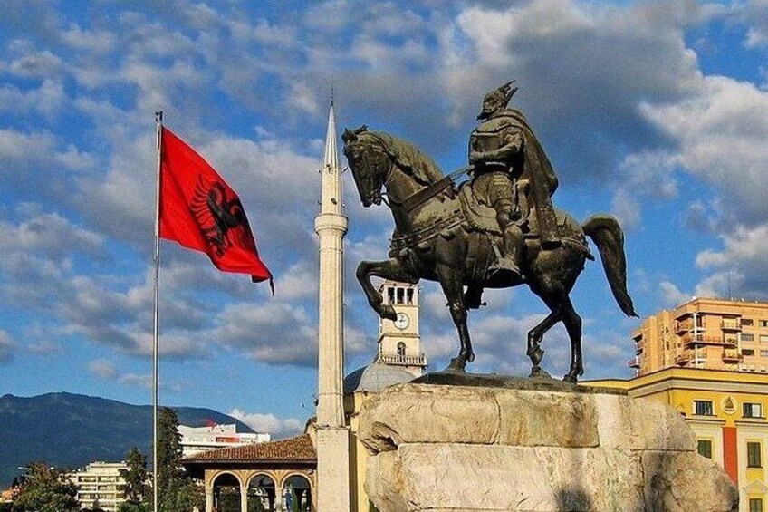 A statue of a person on horseback, a flagpole with a flag, and a building with a tower. 5