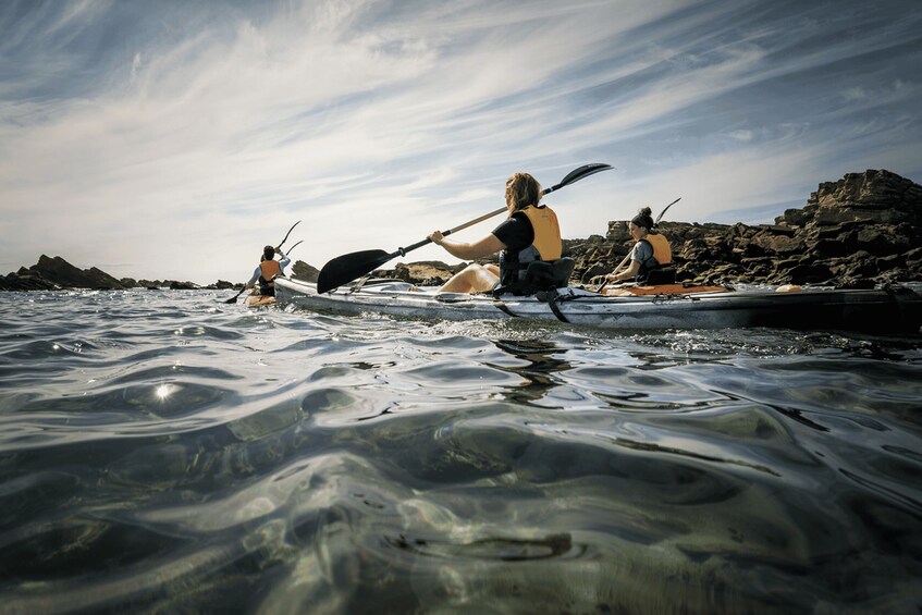 Two kayakers on a calm body of water with rocky shores in the background. 3