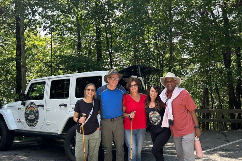 A group of people standing in front of a white off-road vehicle in a wooded area. 5