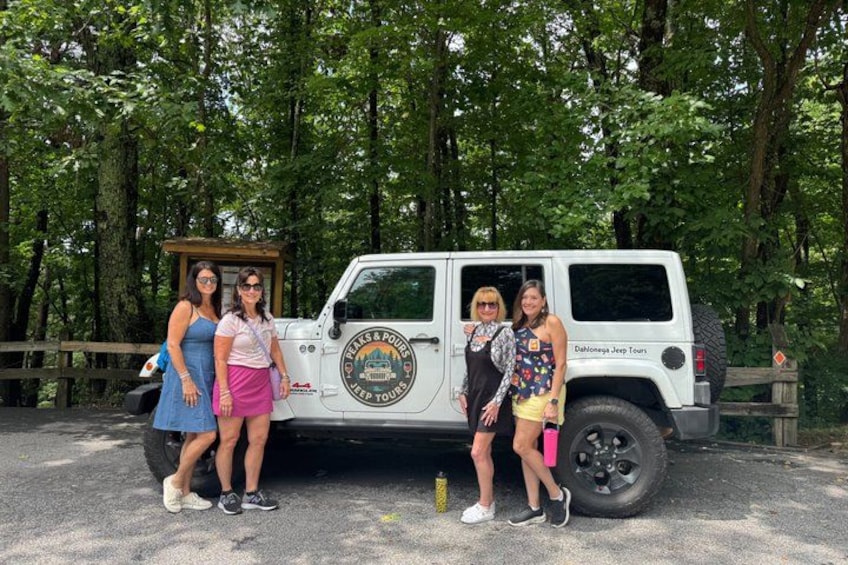 A white Jeep with a logo and text on the side parked in a wooded area. 4