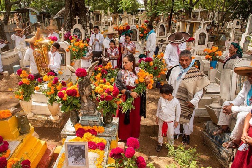 A cemetery with people, flowers, and religious statues. 1