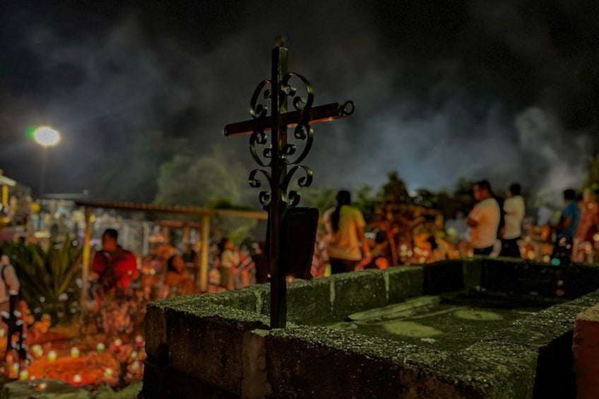 A cross with intricate designs, a stone structure, and a crowd of people in the background. 4