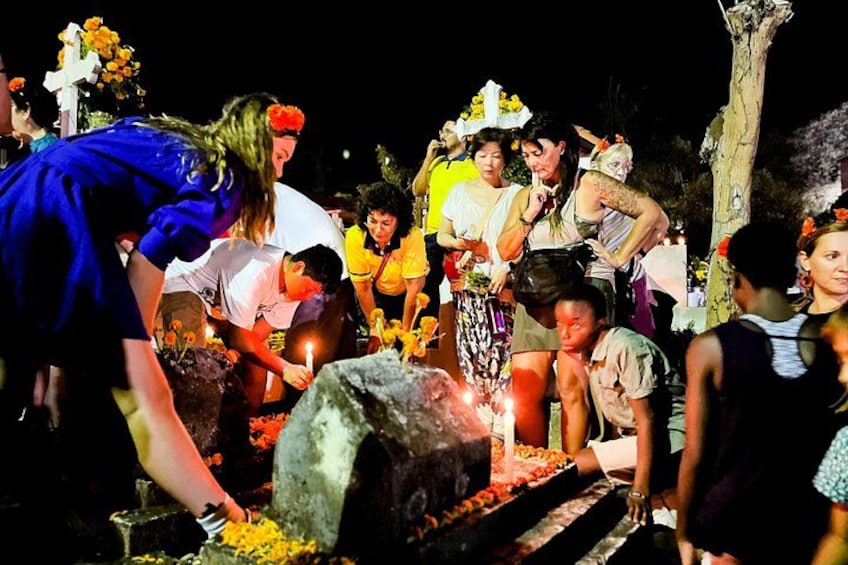 People performing a ritual at a gravesite with candles and flowers. 3
