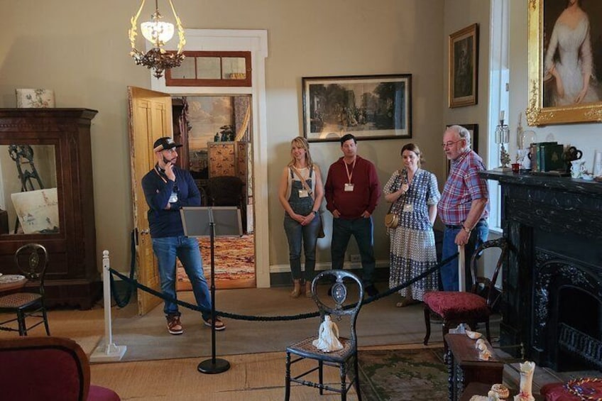 A group of people in a room with a fireplace, a chandelier, and a painting on the wall. 1