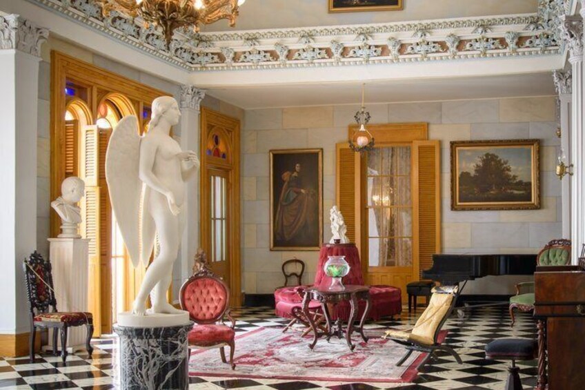 A grand room with a marble statue, red armchairs, and a checkered floor. 2