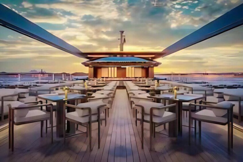 A deck with tables and chairs facing a building with a circular structure, set against a sunset sky. 4