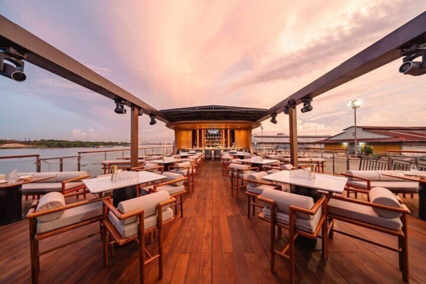 An outdoor restaurant with wooden tables and chairs, a covered seating area, and a view of the water. 3