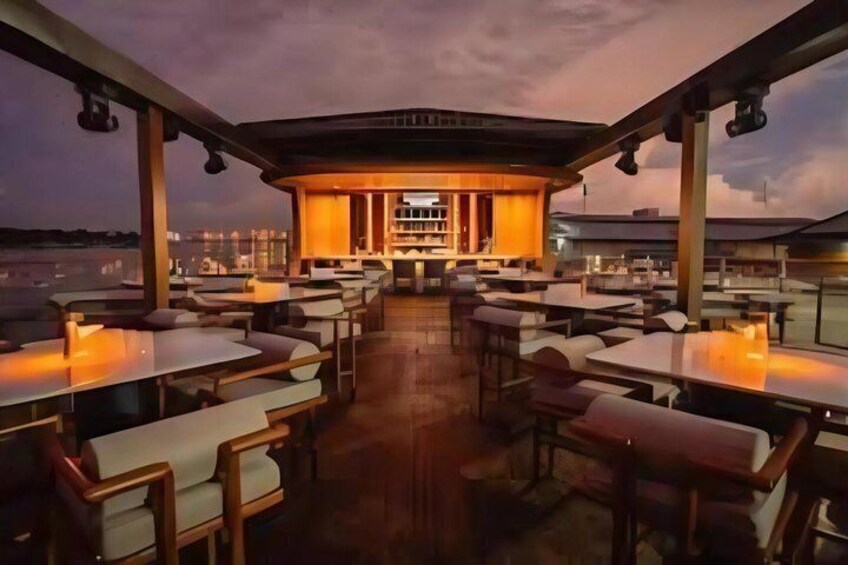 An outdoor restaurant with tables and chairs, a bar area, and a view of the city skyline at dusk. 5