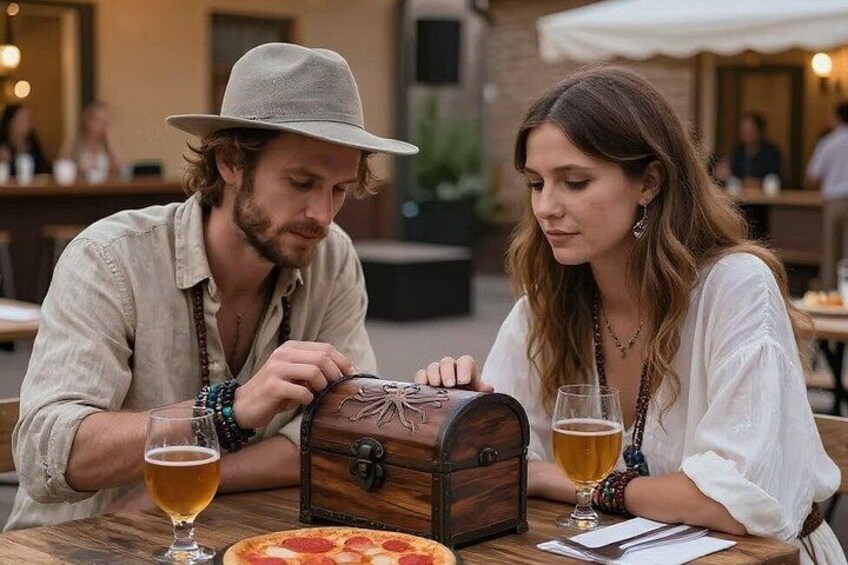 Two people at an outdoor dining table with a pizza and a wooden chest. 2
