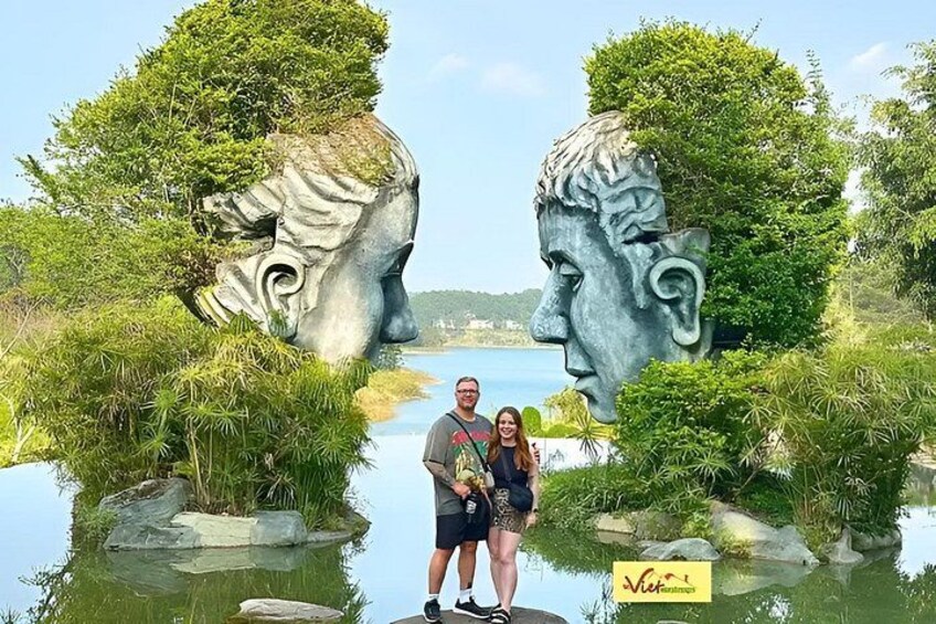 A sculpture of two faces with a body of water between them, surrounded by greenery. 4