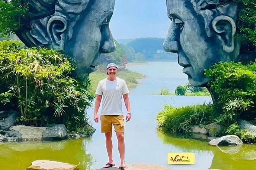 A person standing between two large stone sculptures with a river in the background. 5