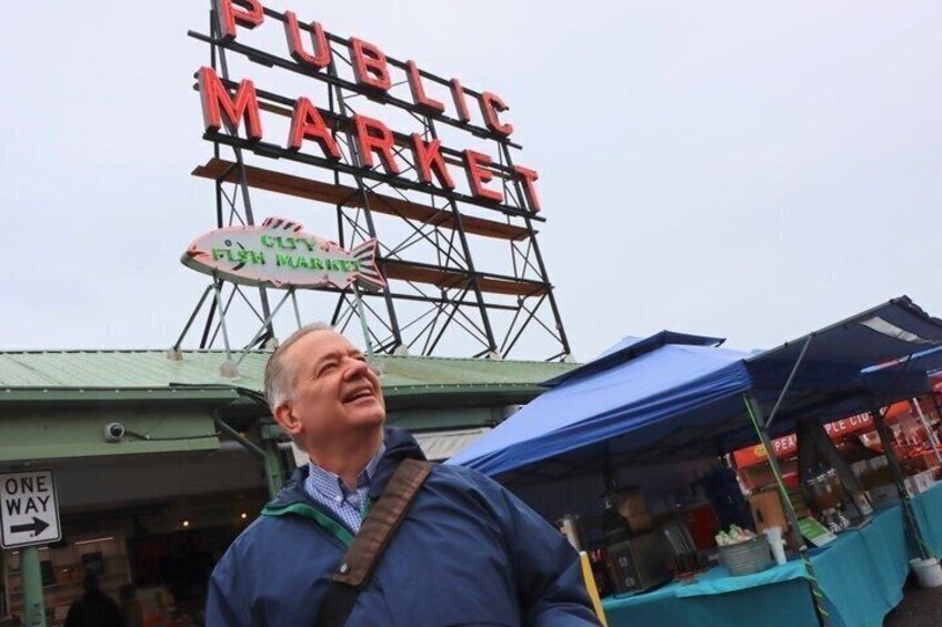A person standing in front of a public market sign. 5