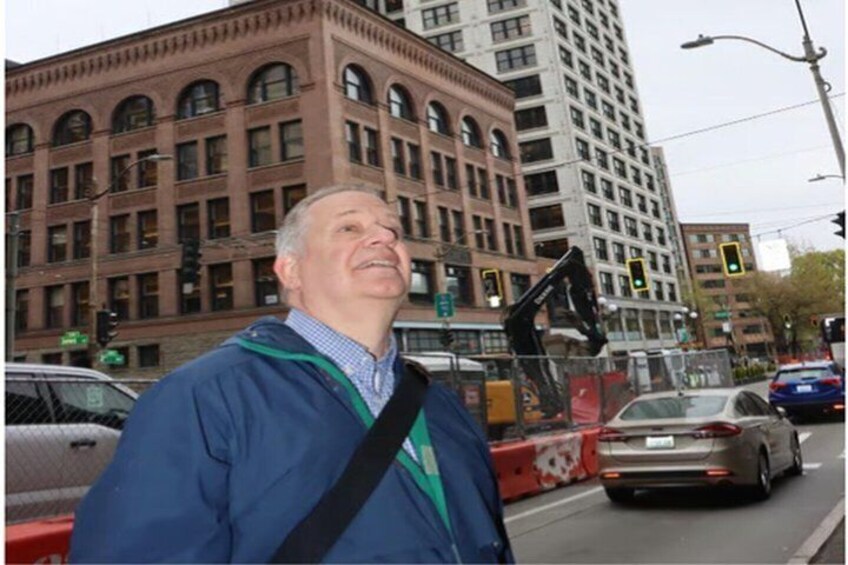 A man in a blue jacket standing on a city street with traffic lights and a tall brick building in the background. 3