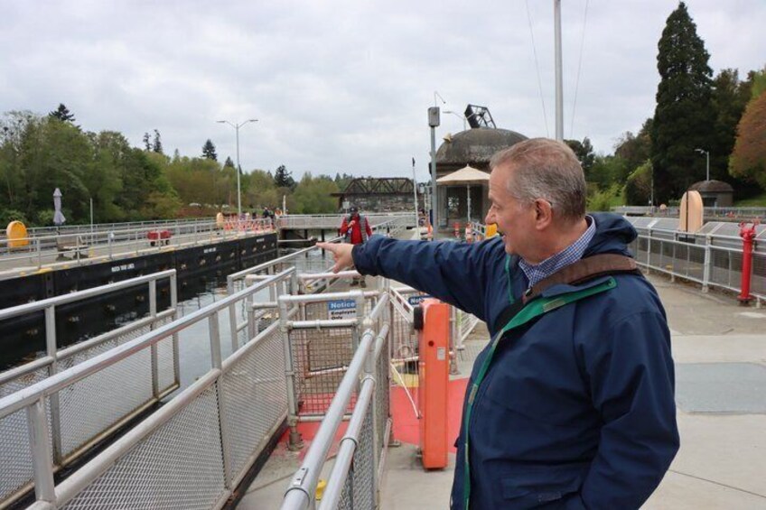A man pointing towards a lock gate on a canal, with a bridge and trees in the background. 1