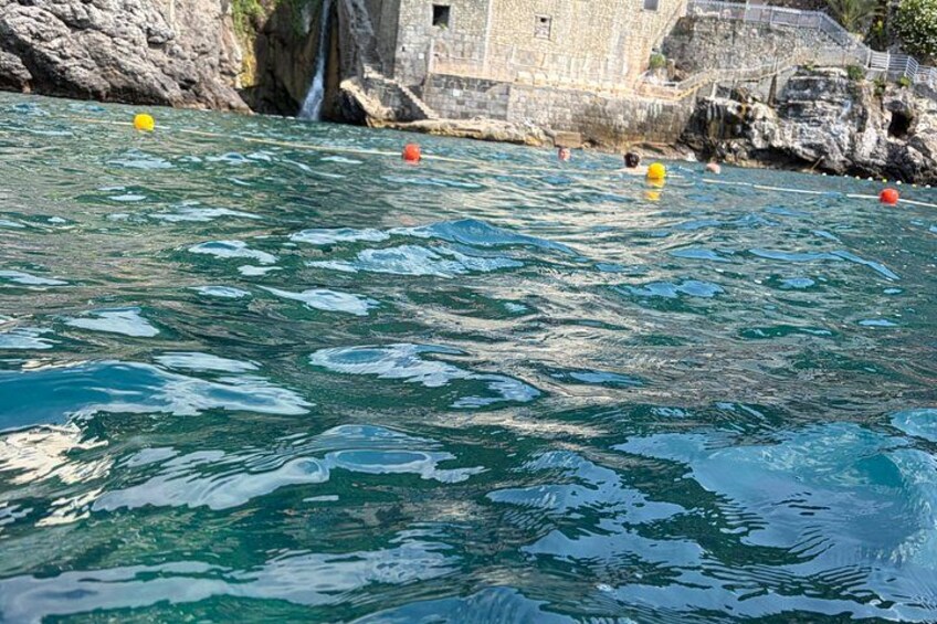 A body of water with clear blue color, a stone building, and a small waterfall. 5